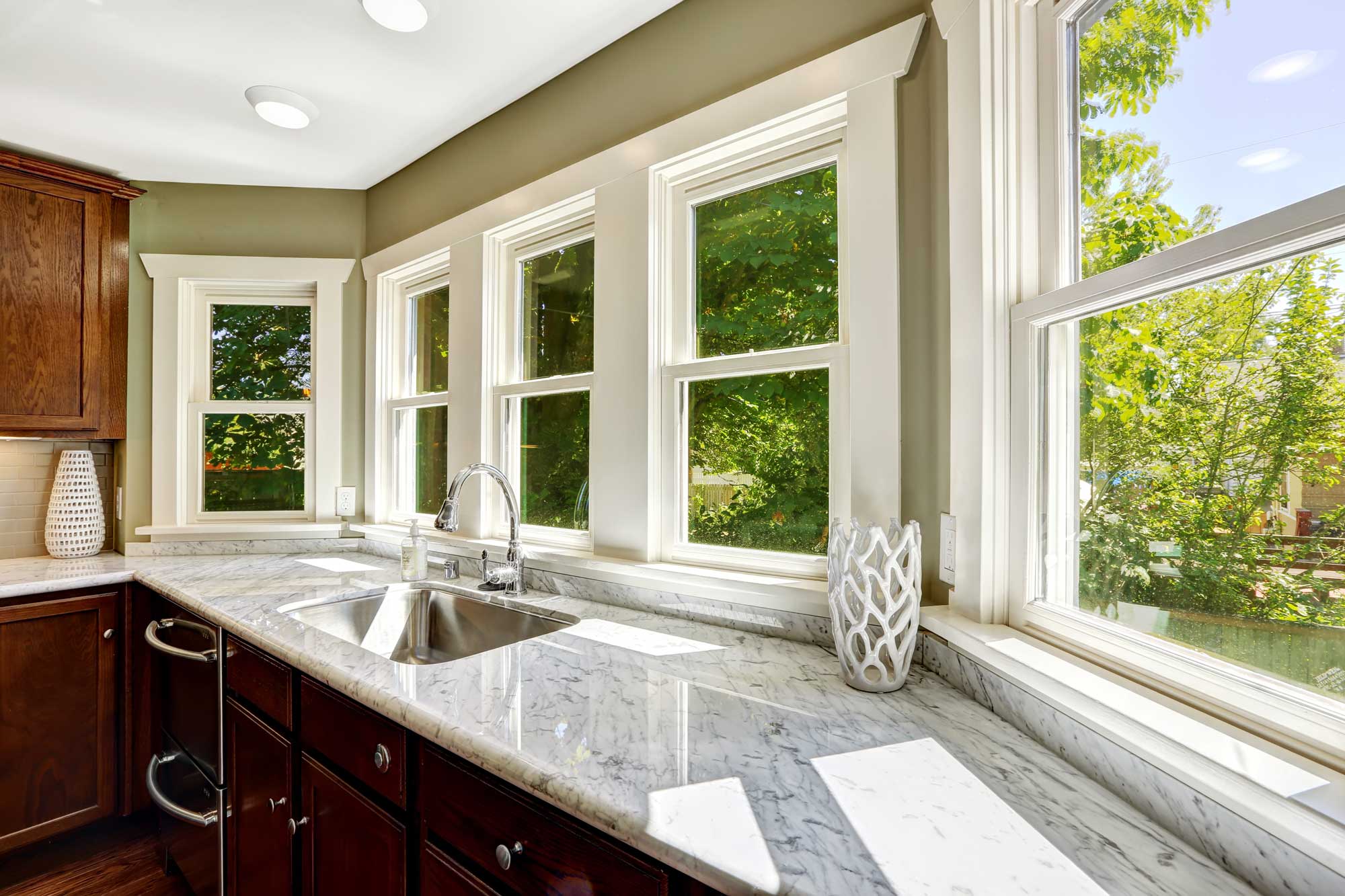 Kitchen countertops under bay windows with view of summer foliage