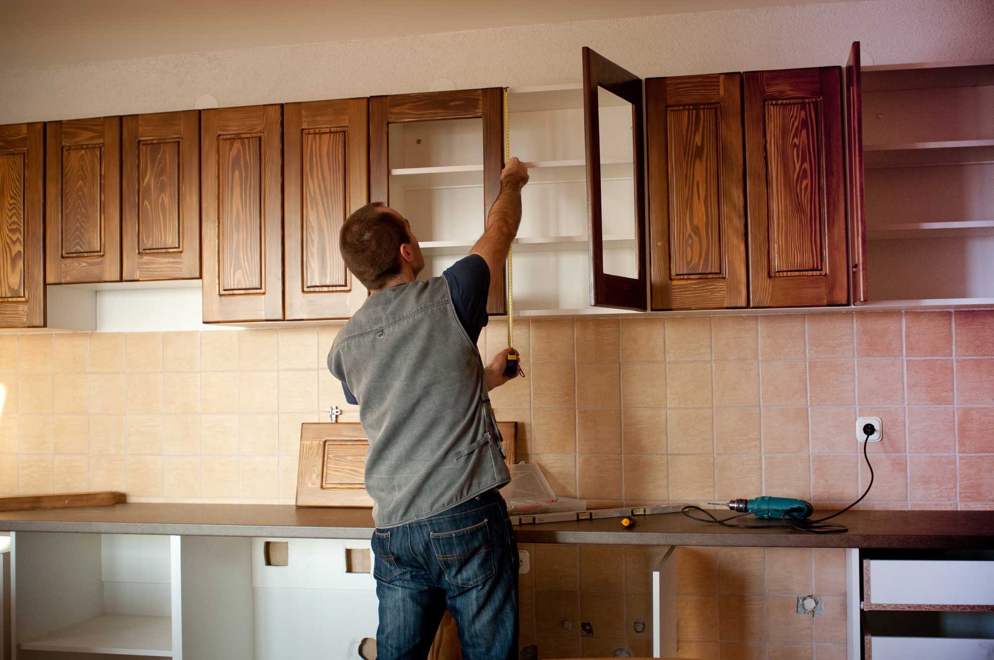 Man measuring wooden cabinet doors in kitchen