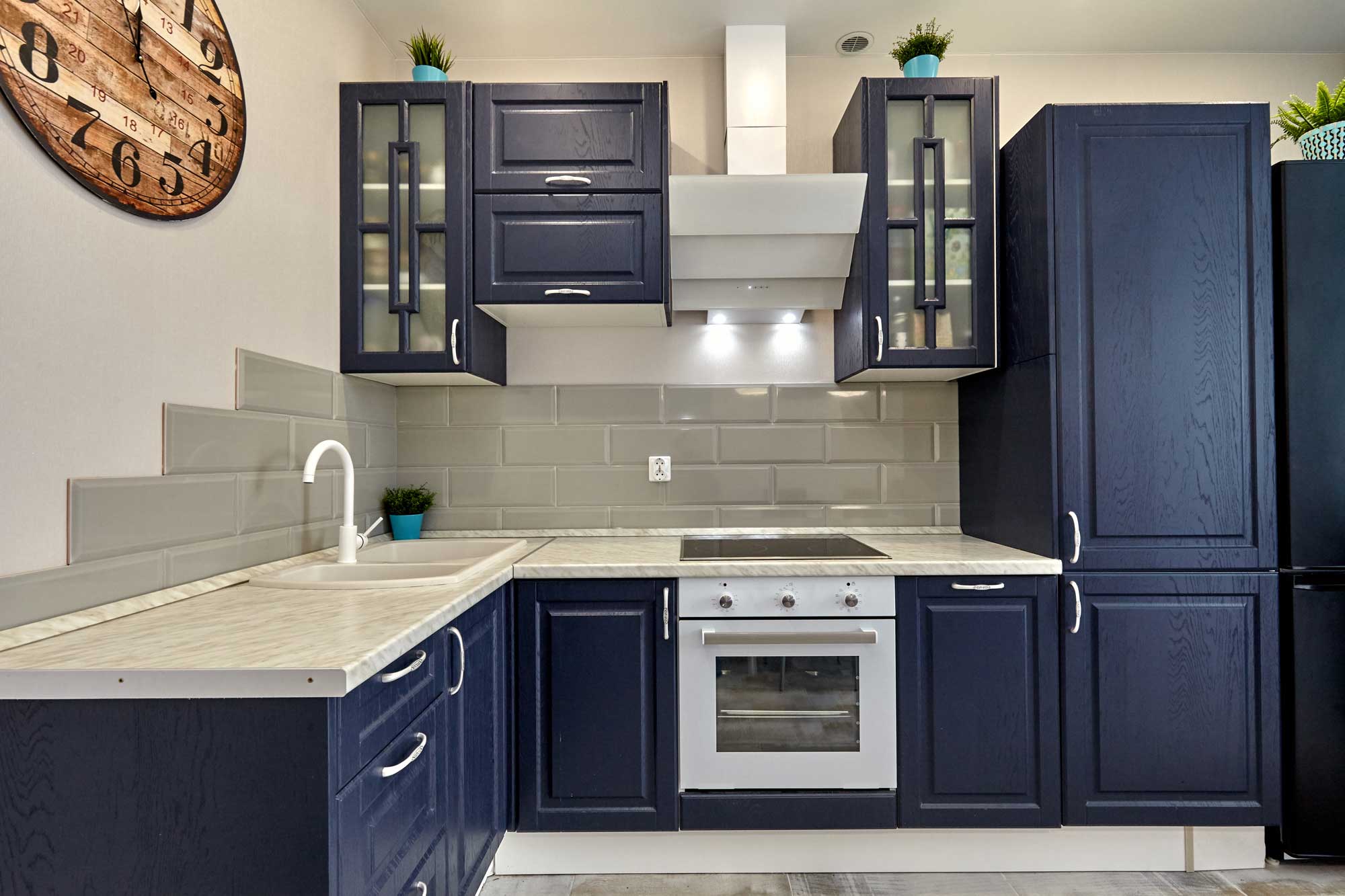 Navy blue painted cabinets in kitchen with gray tile backsplash and clock